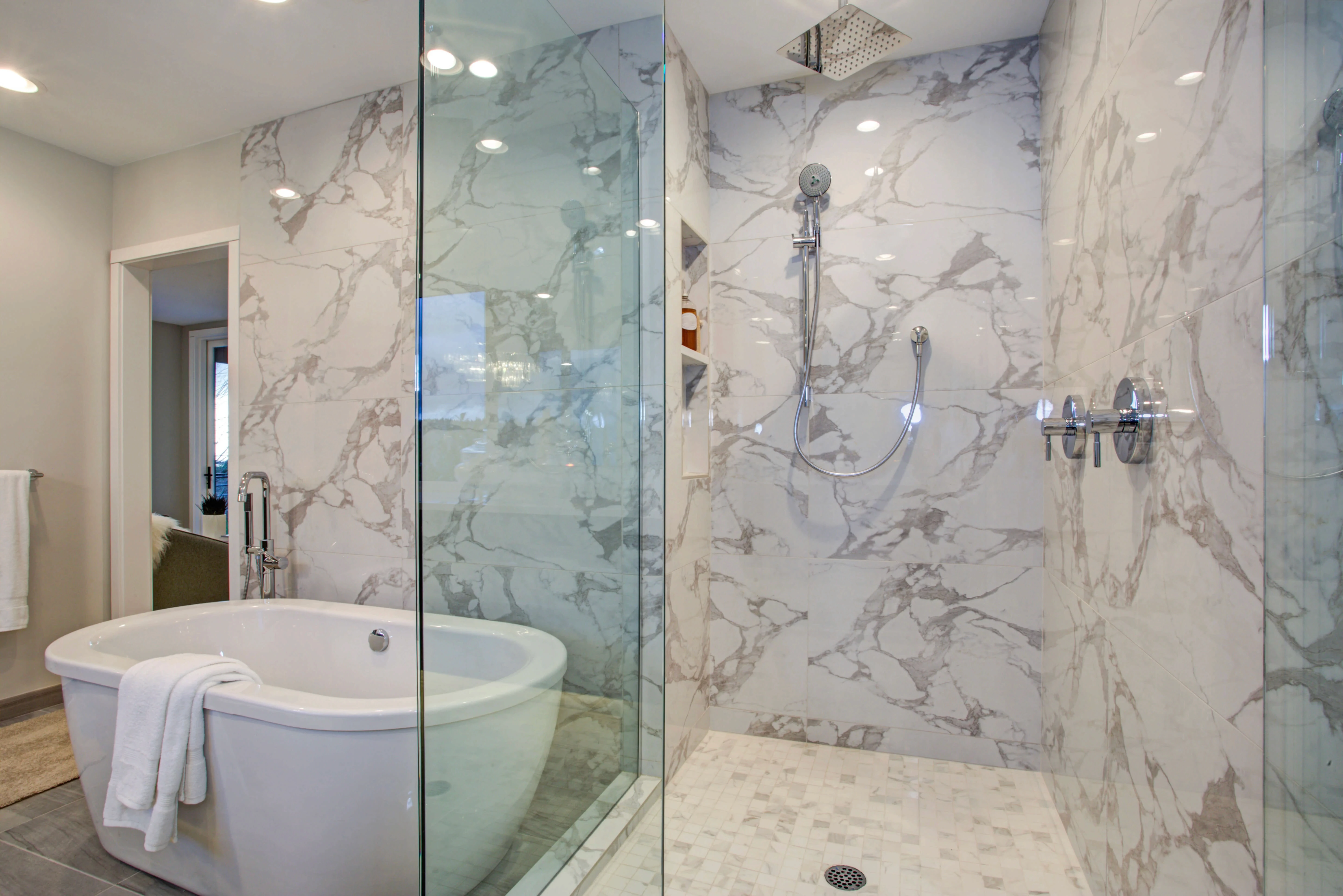 Bathroom with freestanding tub and walk-in shower surrounded by white stone panels with gray veining